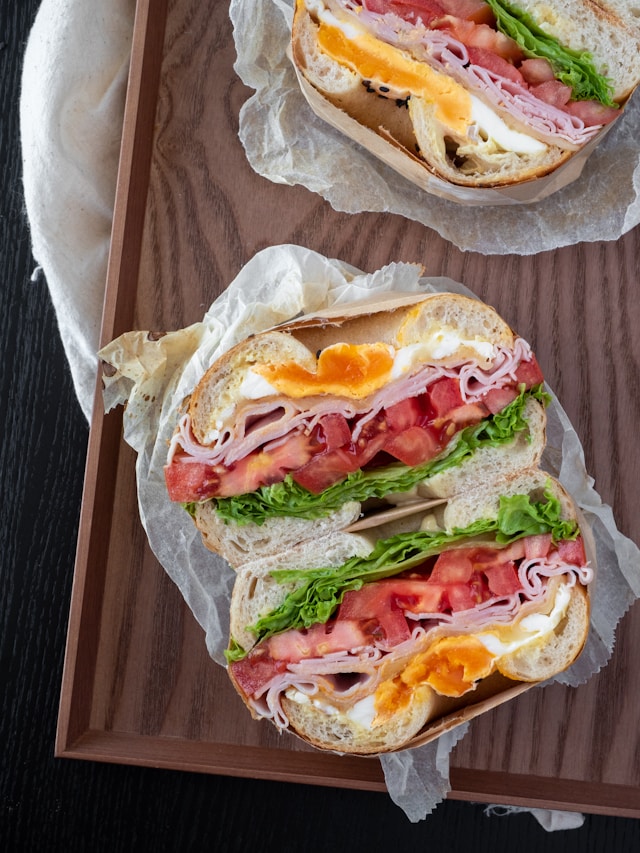 A breakfast bagel containing egg, ham, tomatoes, and lettuce.